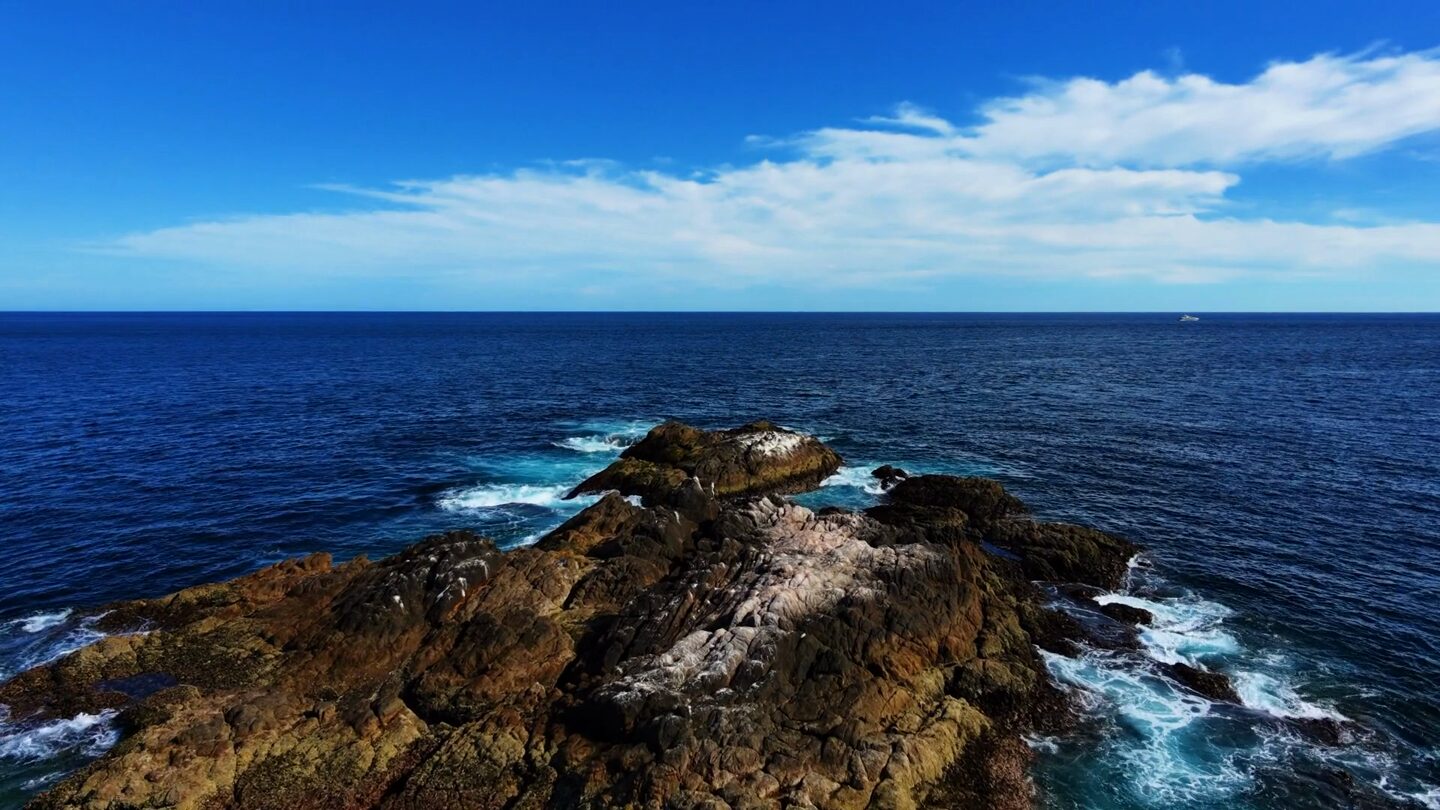 Ilhéu rochoso rodeado de mar azul profundo, visto de cima.